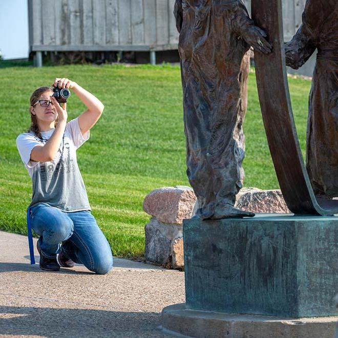 Female photography student taking photo of statue on campus
